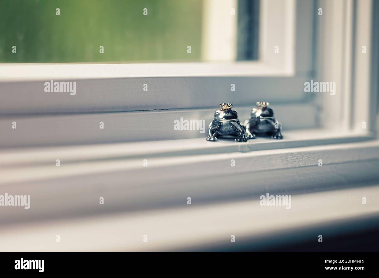 Zwei gekrönte Froschprinz-Figuren aus Sterlingsilber sitzen in der Fensterbank, Konzept der Farbe. Stockfoto