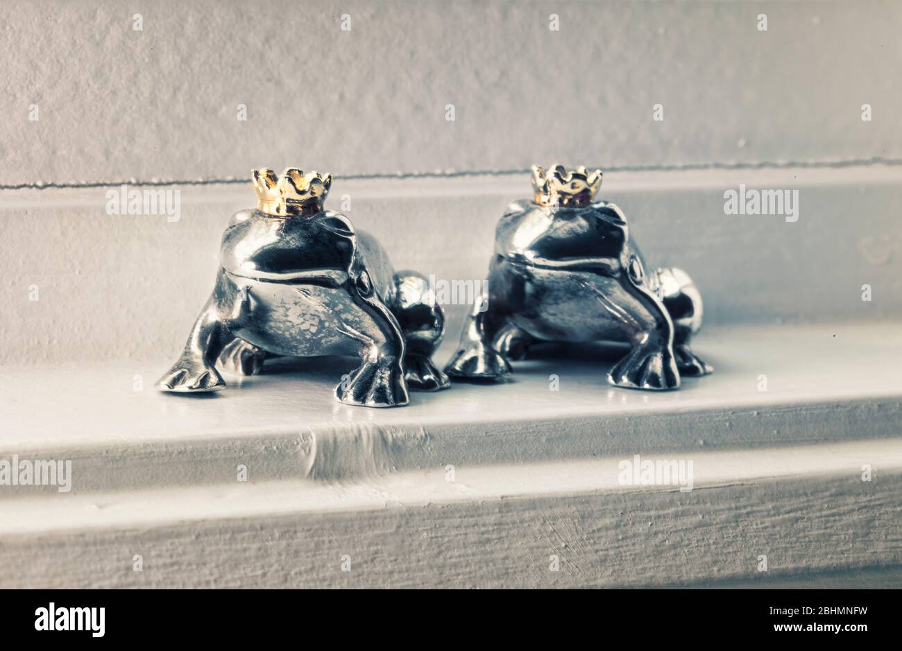 Zwei gekrönte Froschprinz-Figuren aus Sterlingsilber sitzen in der Fensterbank, Konzept der Farbe. Stockfoto