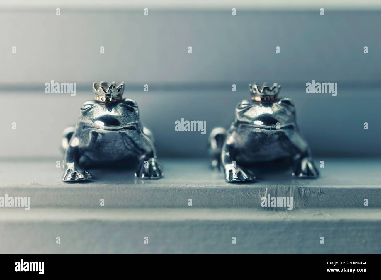 Zwei gekrönte Froschprinz-Figuren aus Sterlingsilber sitzen in der Fensterbank, Konzept der Farbe. Stockfoto