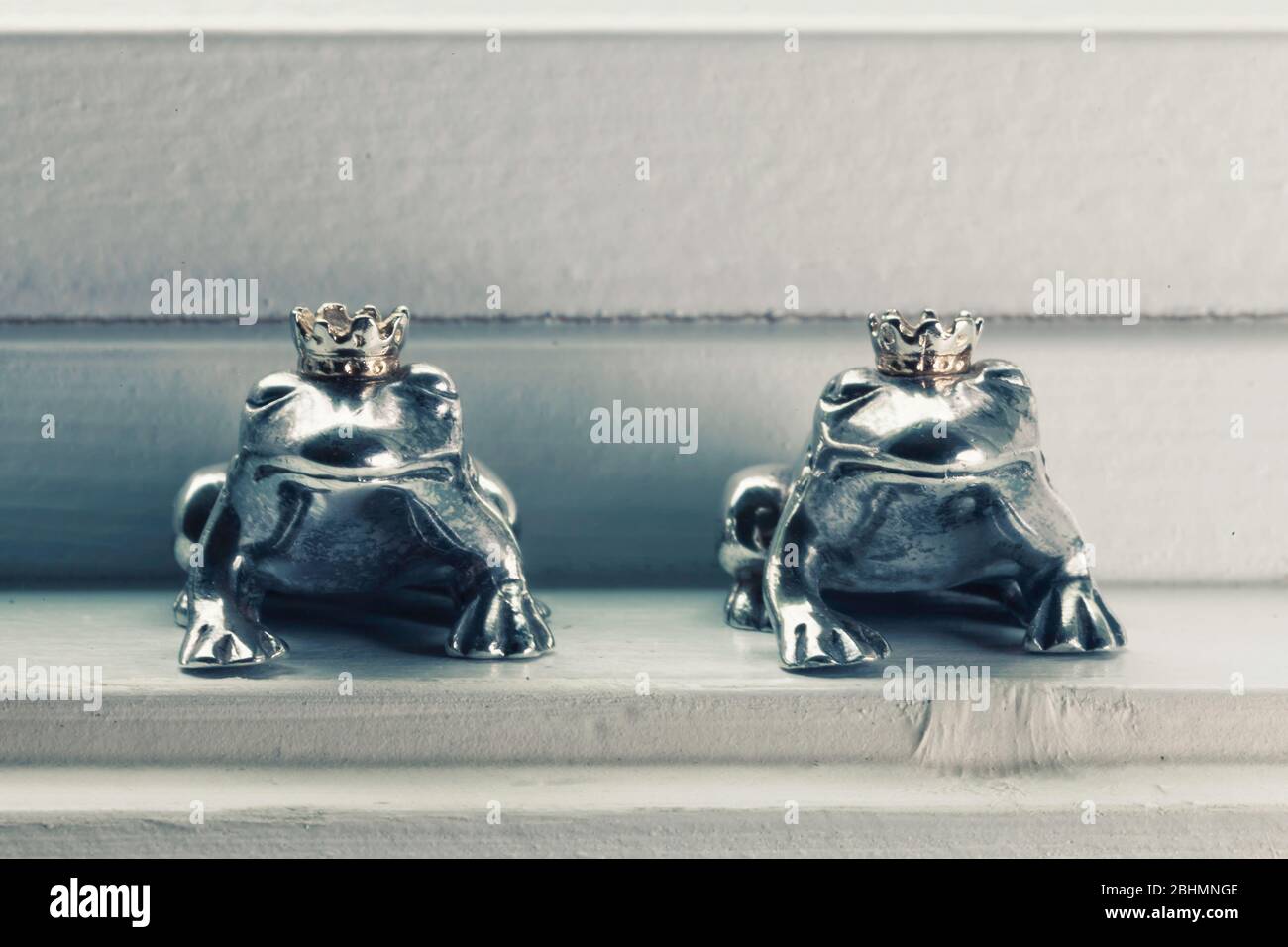 Zwei gekrönte Froschprinz-Figuren aus Sterlingsilber sitzen in der Fensterbank, Konzept der Farbe. Stockfoto