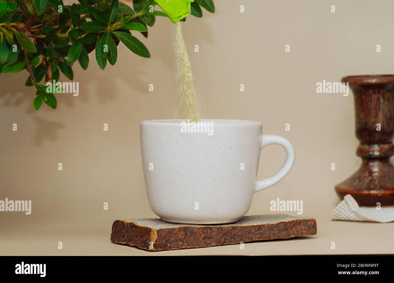 Grüner Matcha-Tee wird in einen weißen Betonbecher auf einem Natursteinständer gegossen. Ein heller Ort für Tee mit einer selbst gewachsenen grünen Pflanze. Stockfoto