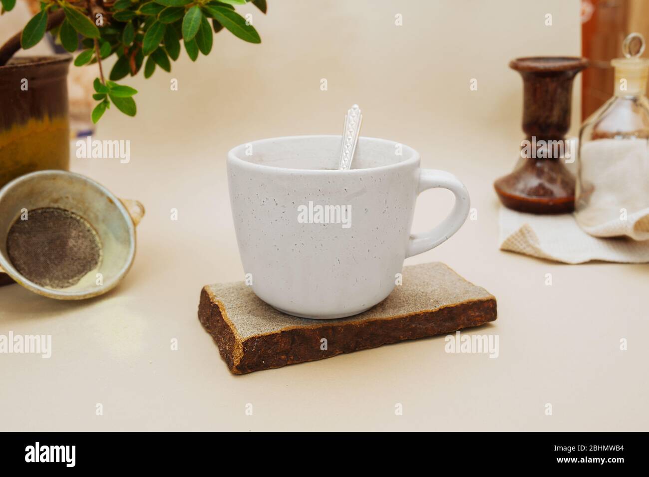 Gemütliches Zuhause Arbeitsplatz oder Mittagessen mit einer Tasse Tee auf einem Naturstein-Ständer, alte Siev, grüne Hauspflanze, Vintage-Metall-Löffel. Stockfoto