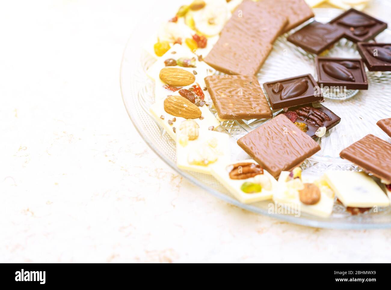 Set von verschiedenen Broken handgemachte Schokolade Stücke mit Nüssen, getrockneten Beeren, Preiselbeeren in einem Teller auf weißem Hintergrund. Overhead-Ansicht, Kopierbereich. Stockfoto