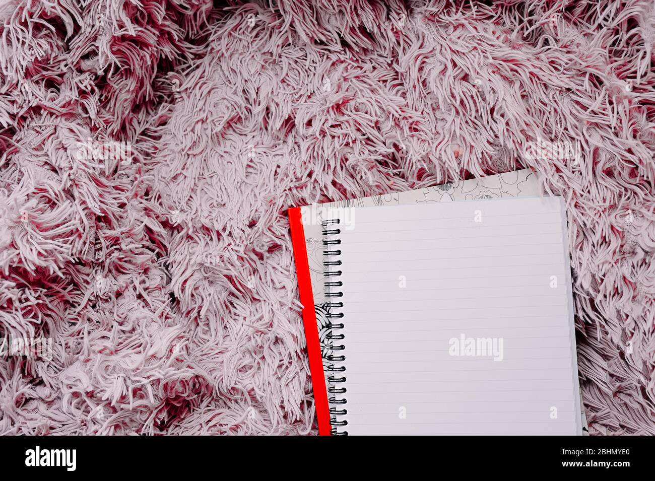 Öffnen Sie ein leeres großes Notizbuch auf einer Spirale auf einer rosa, flauschigen Decke. Stockfoto