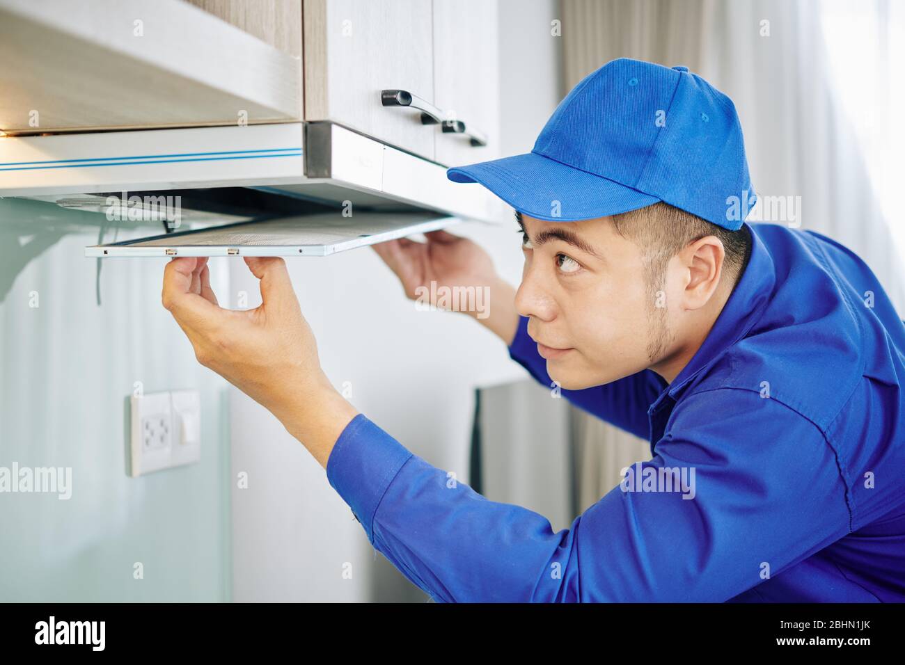 Handwerker in blauer Uniform Einbau oder Reparatur Dunstabzugshaube in der  Küche des Kunden Stockfotografie - Alamy