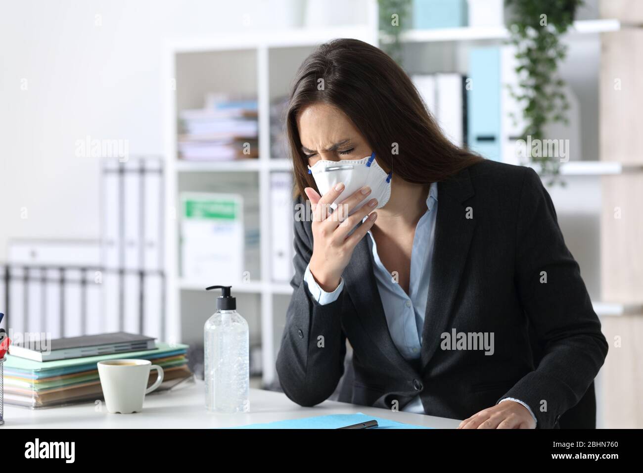 Exekutive Frau mit Maske hustet und niest auf einem Schreibtisch im Büro Stockfoto