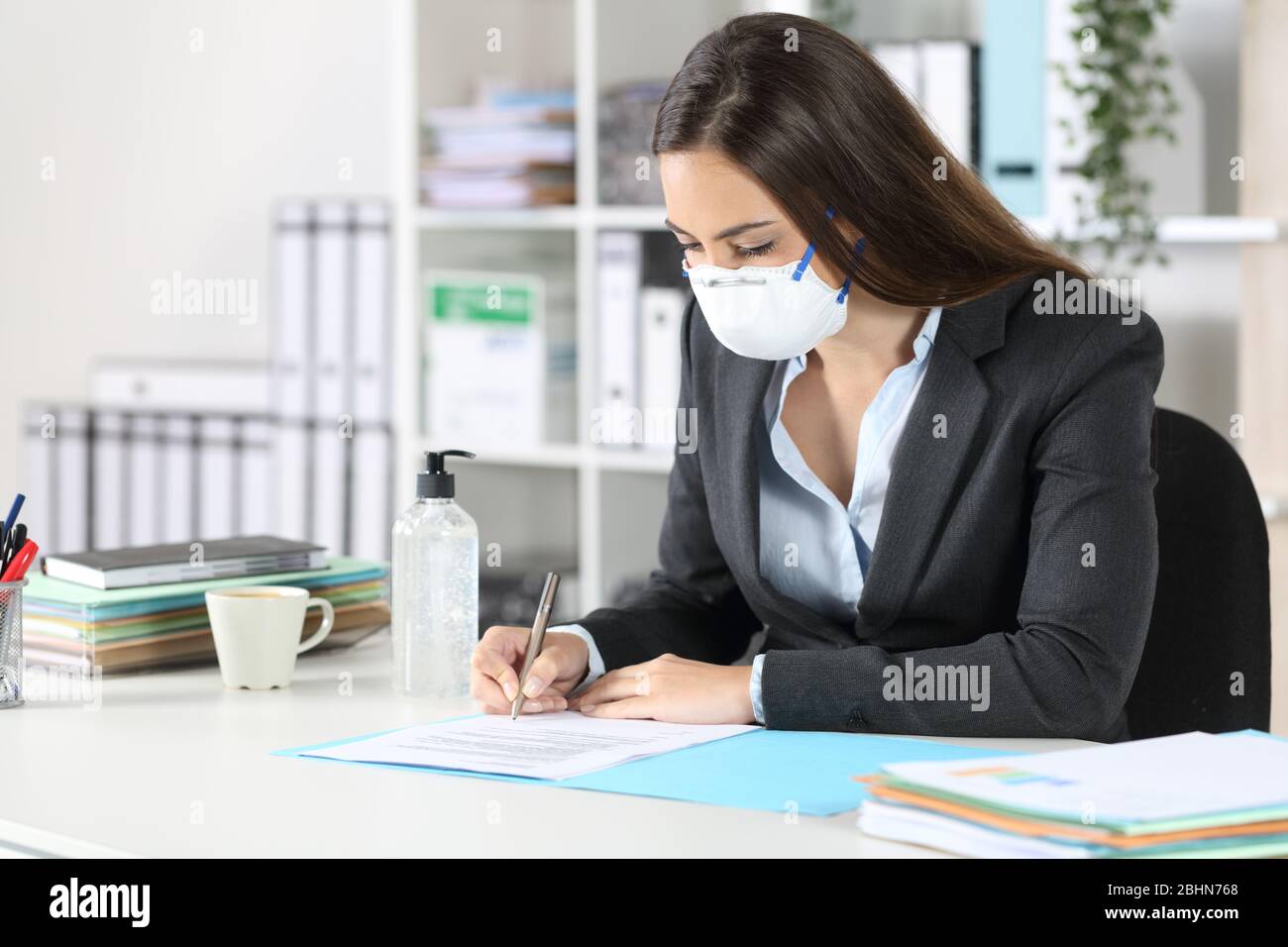 Exekutive Frau mit Schutzmaske Vermeidung Coronavirus Unterzeichnung Vertrag an ihrem Schreibtisch im Büro Stockfoto