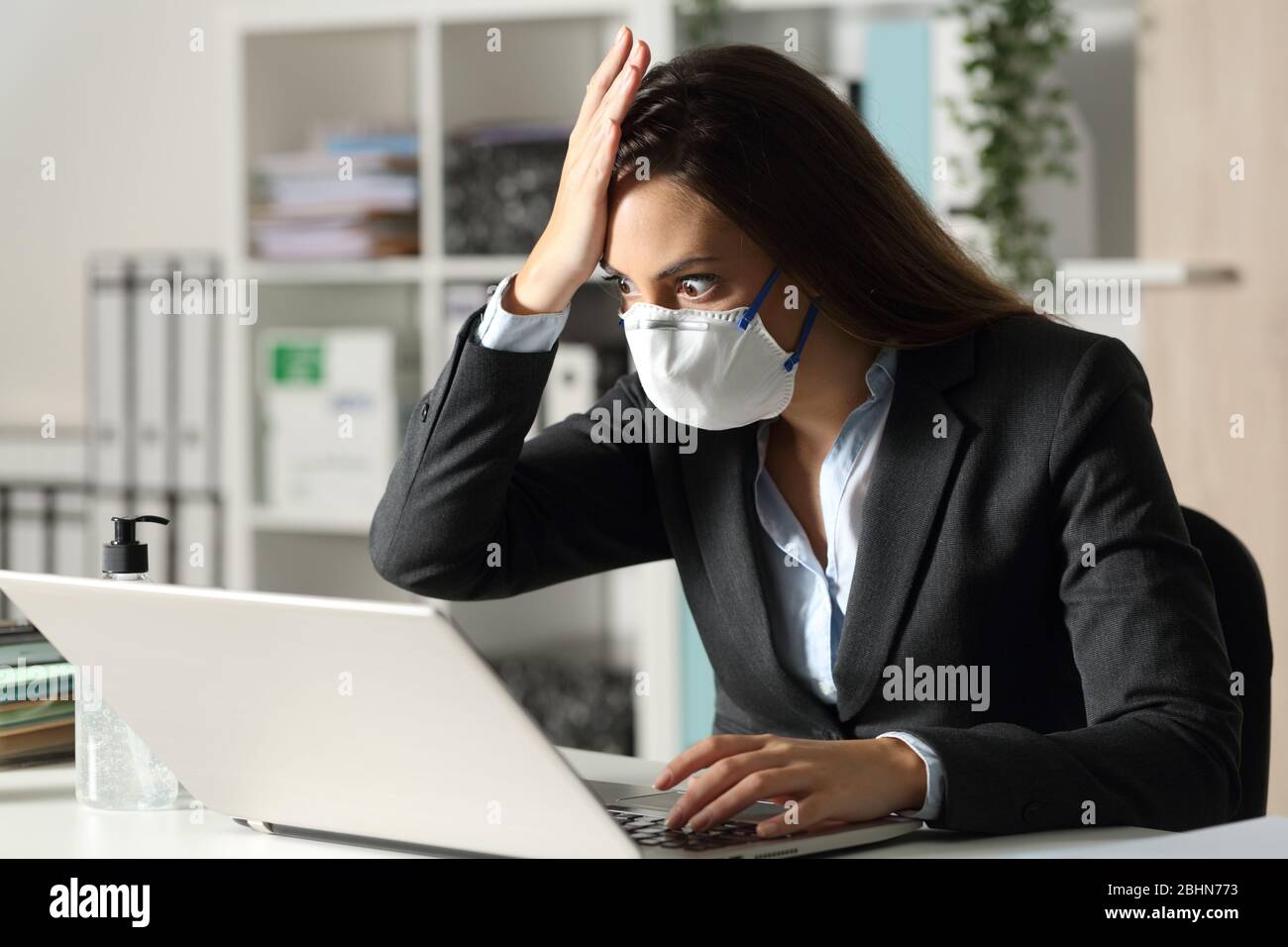 Überraschte Exekutive Frau mit Schutzmaske findet Fehler auf Laptop in der Nacht in der ofice Stockfoto
