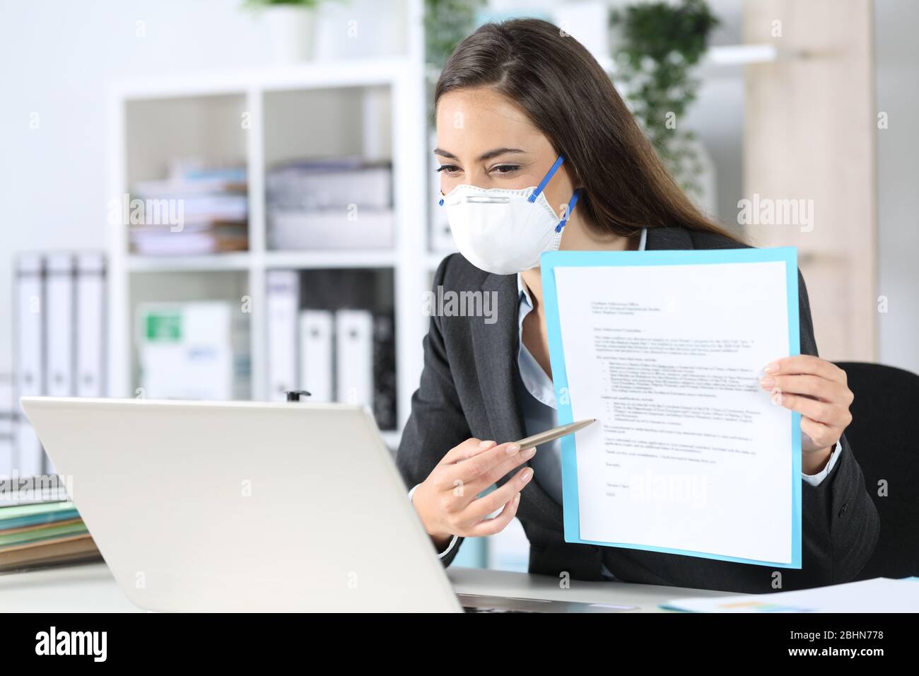 Executive Frau mit Schutzmaske zeigt Vertrag auf Videocall auf Laptop im Büro Stockfoto