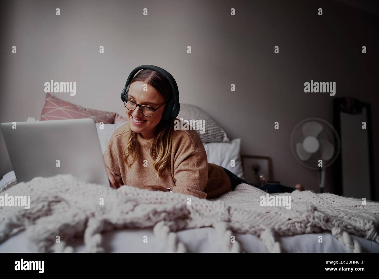 Junge Frau mit Brille, die Kopfhörer trägt, Musik hört und Online-Kurse besucht - junge Studentin bei einem Online-Videoanruf Stockfoto
