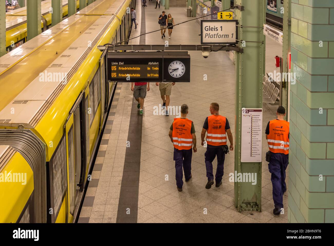 Drei Männer des Berliner Verkehrsunternehmens BVG in orangen, gut sichtbaren Westen auf einer Plattform der Berliner U-Bahn. Rückansicht der Personen Stockfoto