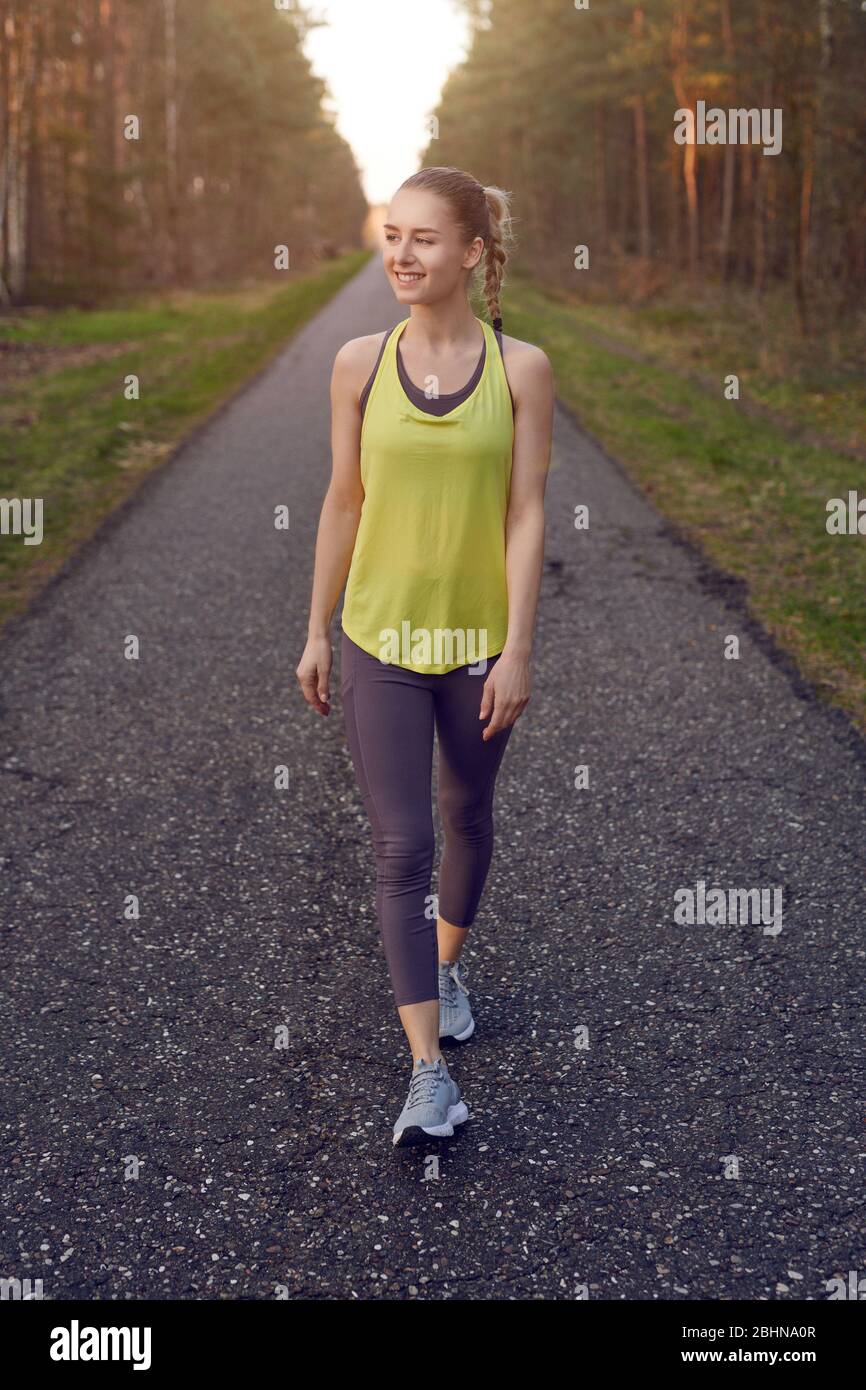 Lächelnde, sportliche Passform junge Frau, die auf einer geteppelten Spur durch Wälder arbeitet, die durch das warme Leuchten der Sonne in einem gesunden, aktiven Lifestyle-Schein beleuchtet werden Stockfoto