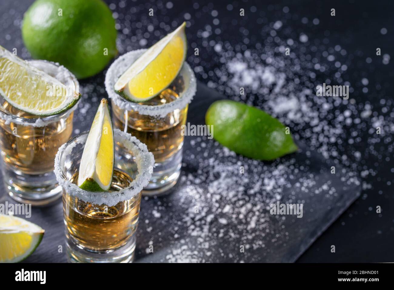 Tequila mit Limette auf einem dunklen Tisch mit Salz bestreut Stockfoto