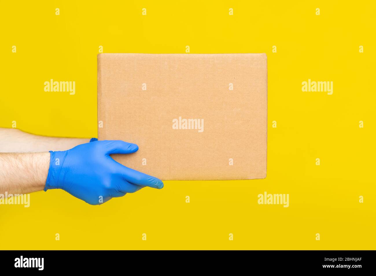 Nahaufnahme Hände Lieferung Mann medizinische Handschuhe halten leere Karton auf gelben Studio Hintergrund. Service Coronavirus. Online-Shopping. Mock up. Stockfoto