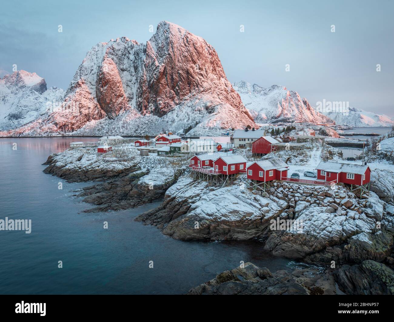 Atemberaubender Sonnenaufgang in Hamnoy - beliebtes Reiseziel. Erstes Licht auf schneebedeckten Bergen und roten traditionellen Häusern im Fischerdorf. Kalter Sieg Stockfoto