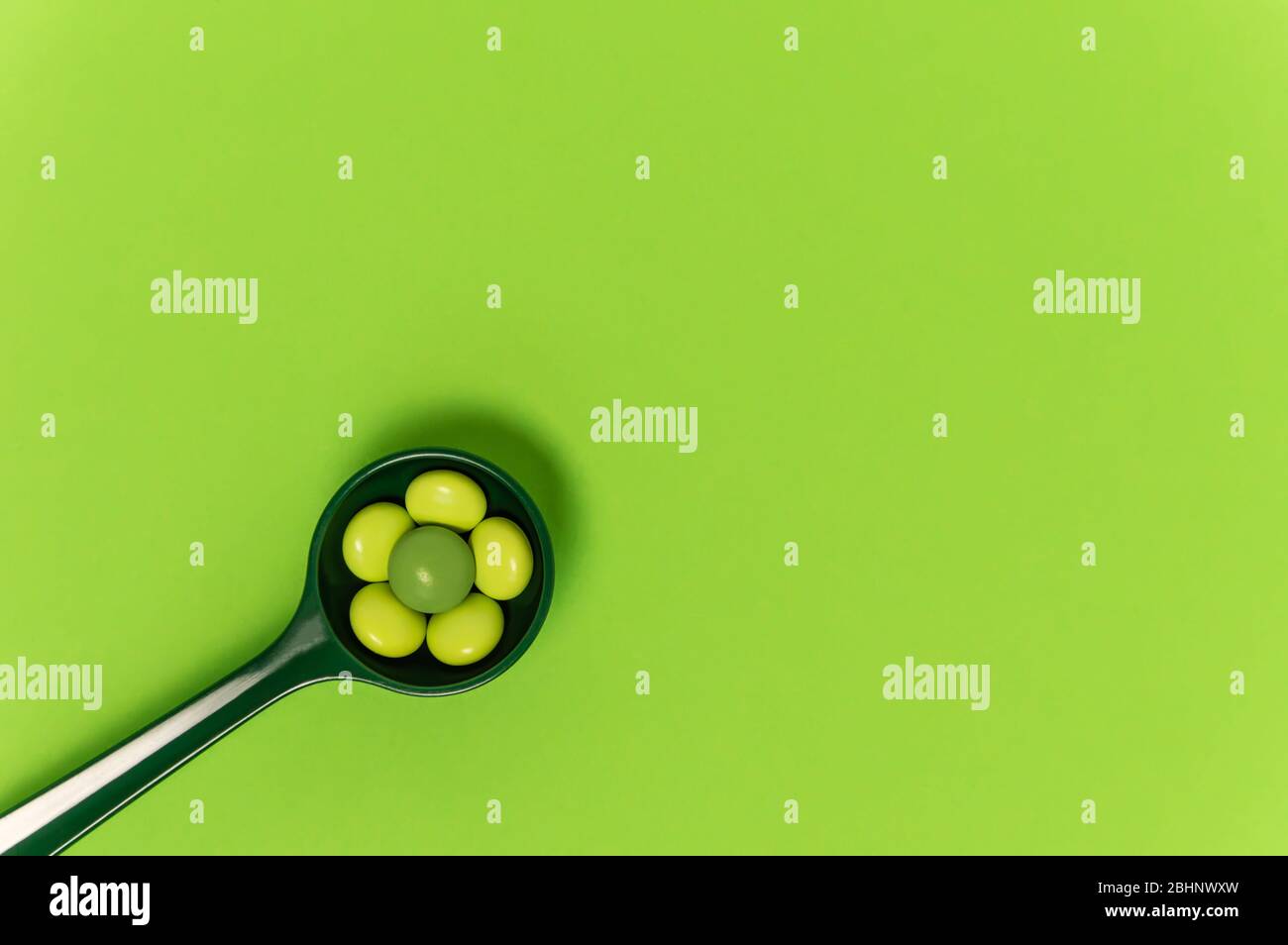 Löffel mit Bio-grünen Pillen auf grünem Hintergrund. Medizin Dosis von Nahrungsergänzungsmitteln oder verschreibungspflichtige Medikamente für die Krankheitstherapie. Pharmazeutik Stockfoto