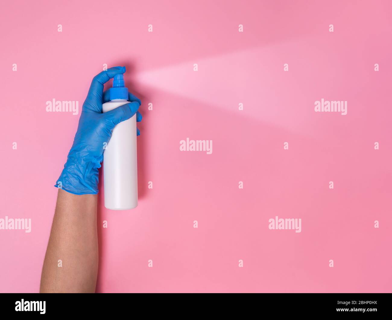 Schutz vor Coronavirus. Hand in blauen Einweg-Handschuh übersprühen Oberfläche Desinfektionsmittel oder Hand Desinfektionsmittel in weißen Sprühflasche auf rosa Hintergrund. Hy Stockfoto