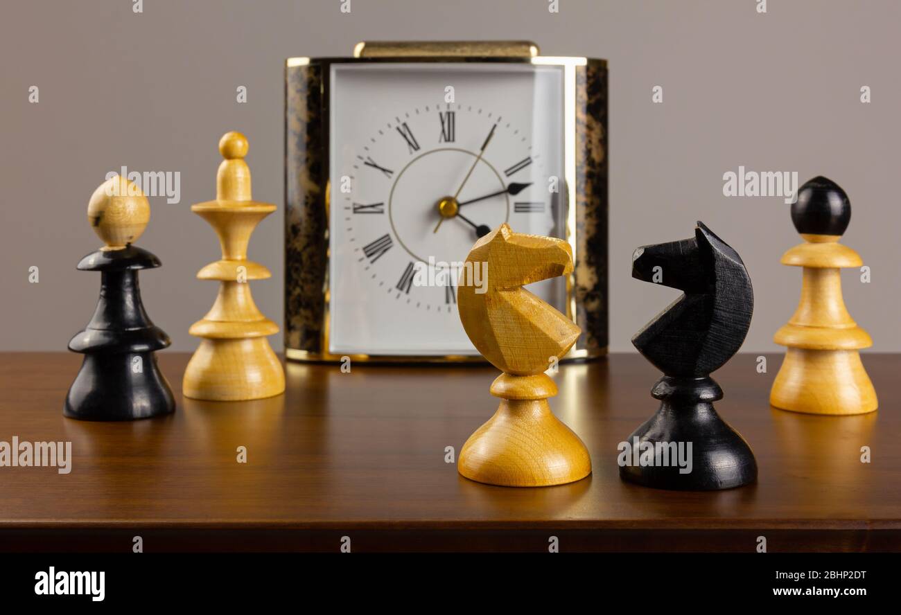 Zwei Ritter stehen einander auf einem Holztisch gegenüber, mit einem Wecker und anderen Schachfiguren im Hintergrund Stockfoto