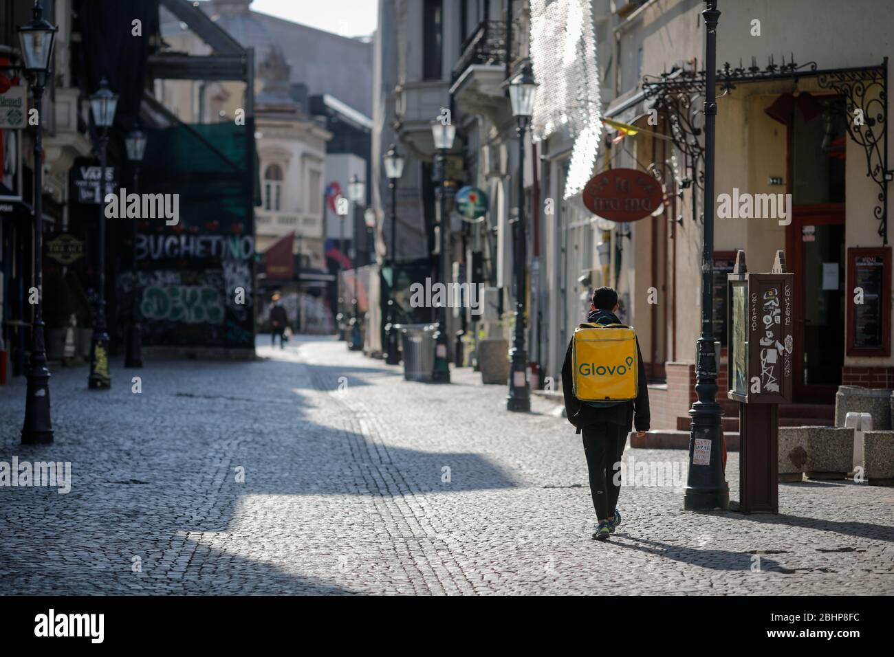 Bukarest, Rumänien - 22. April 2020: Mann, der während der Blockade des Covid-19 einen Glovo-Lieferrucksack auf den leeren Straßen der Altstadt von Bukarest trägt. Stockfoto