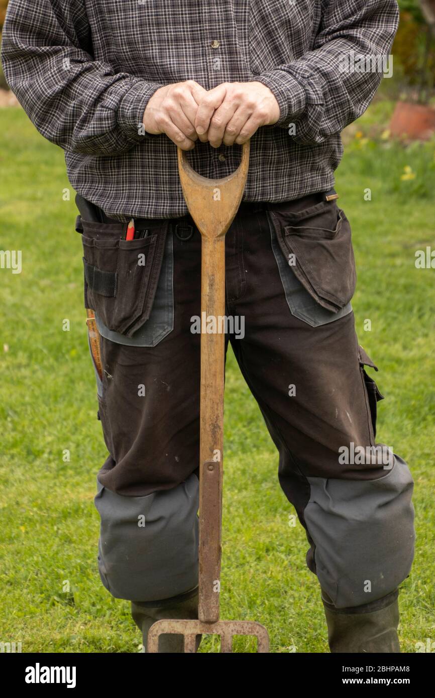 Die Hände eines Mannes ruhen auf dem Griff einer Gartengabel Stockfoto