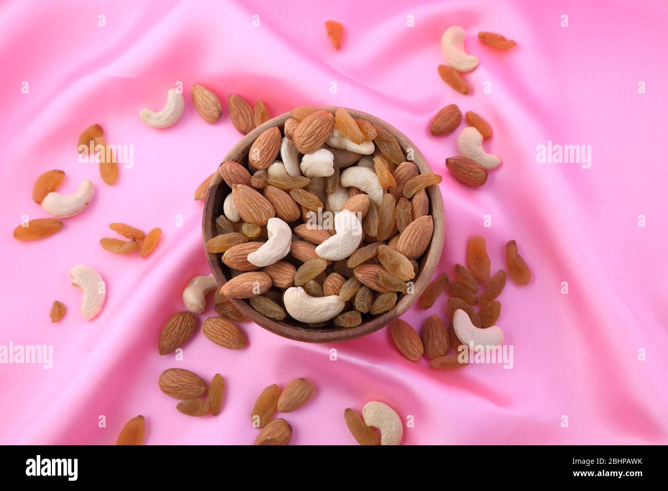 Köstliche und gesunde gemischte Trockenfrüchte, Nüsse und Samen in einer Holzschale auf rosa seidigem Hintergrund. Stockfoto