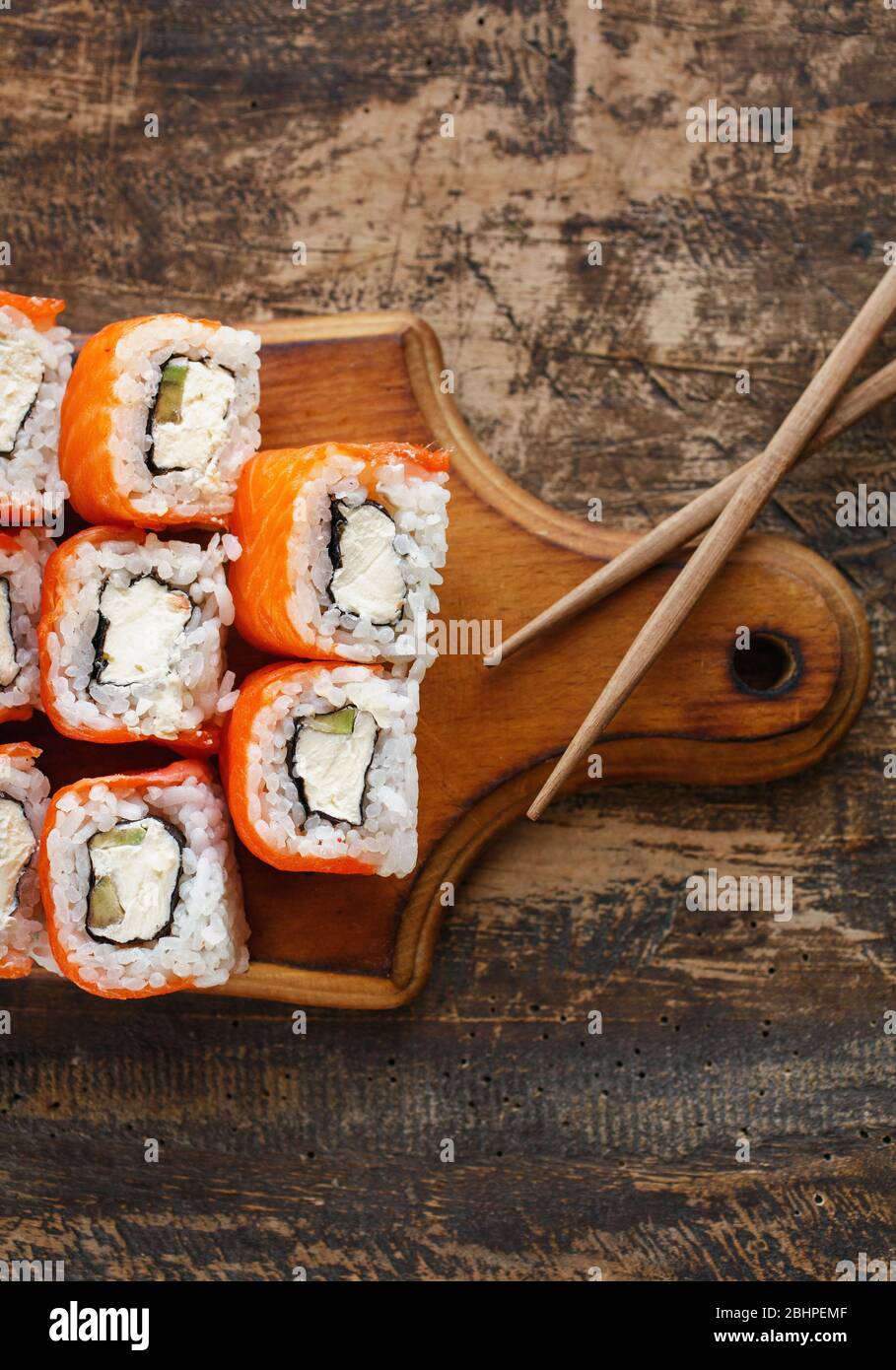 Sushi-Set mit Philadelphia-Käse, Avocado und Lachs auf einem braunen Holzbrett. Stockfoto