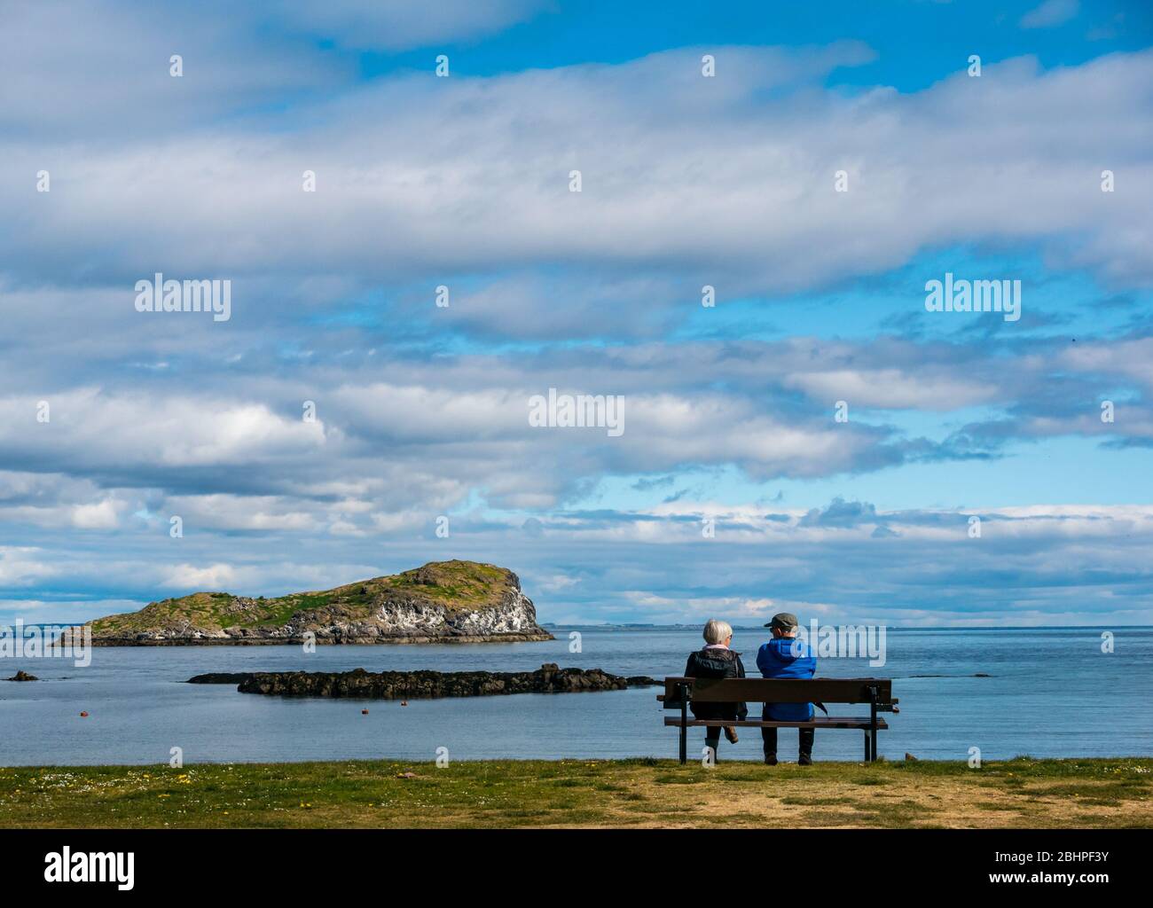 North Berwick, East Lothian, Schottland, Großbritannien. April 2020. UK Wetter: Ein ruhiger heller Tag. Trotz des ruhigen Wetters sind die Strände während der Sperrung fast leer. Ein Paar ruht sich auf einer Bank mit Blick auf den Firth of Forth und Craigleith Island in West Bay aus Stockfoto