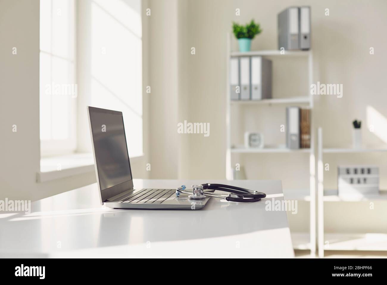 Arzt online. Ein Stethoskop befindet sich auf einem weißen Tisch mit einem Laptop in Unschärfe im Krankenhaus Büro. Stockfoto