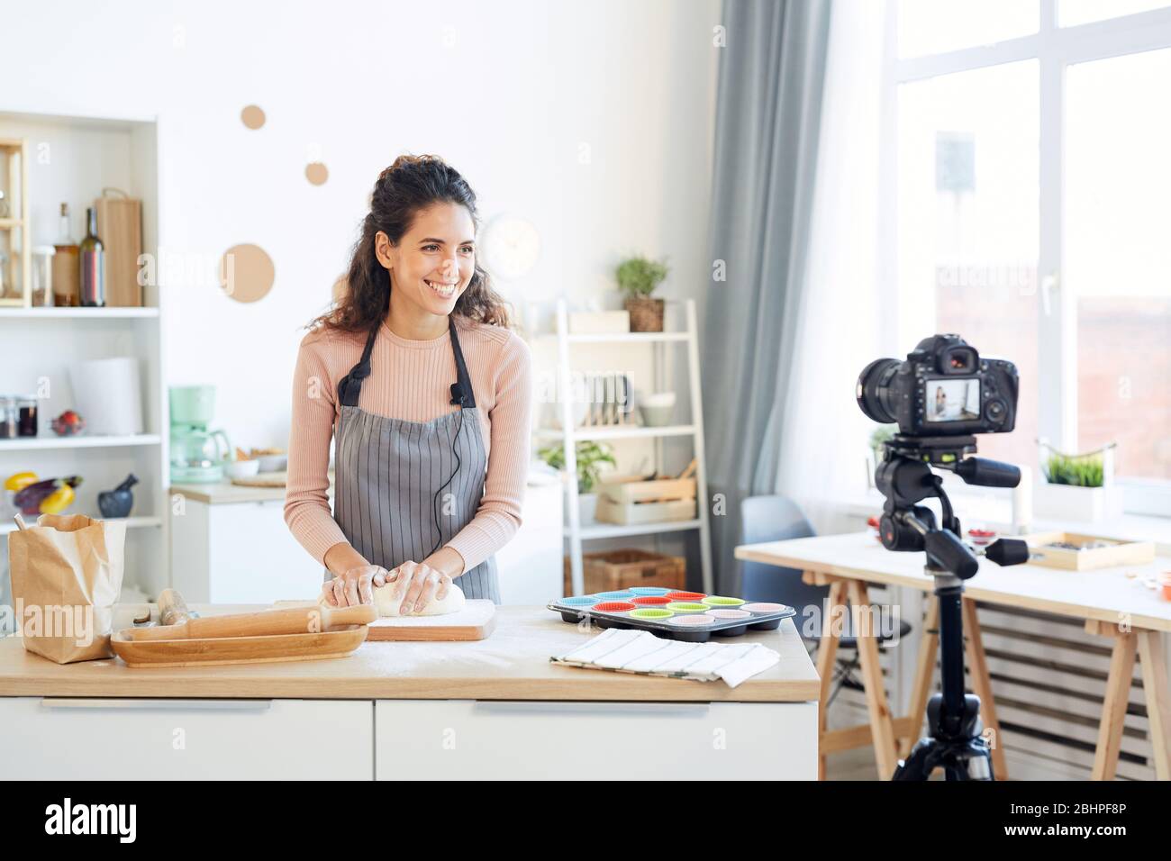 Lächelnde junge Frau Kneten Teig für Cupcakes während der Aufnahme Video für ihre Lebensmittel-Blog Stockfoto