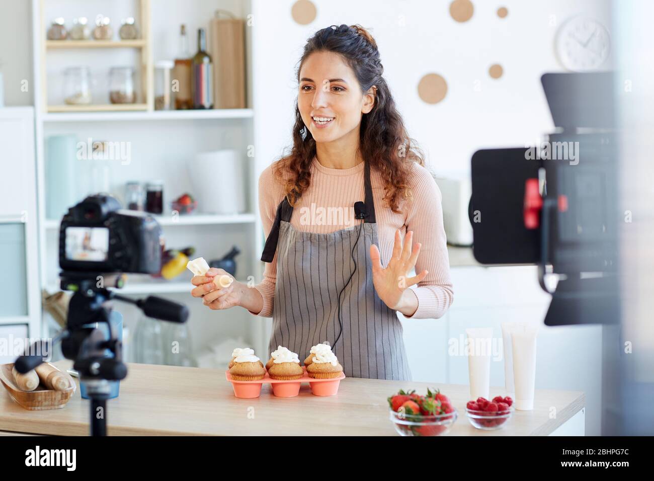 Positive junge Erwachsene Frau schießen hausgemachte Cupcakes Video-Tutorial für ihr Essen Blog-Kanal Stockfoto