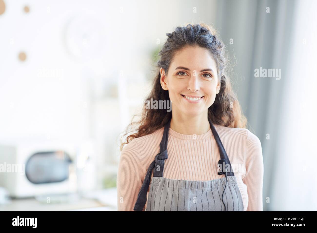 Stilvolle kaukasische Frau trägt Schürze stehend in der Küche Blick auf Kamera lächelnd, horizontale Brust nach oben geschossen Stockfoto