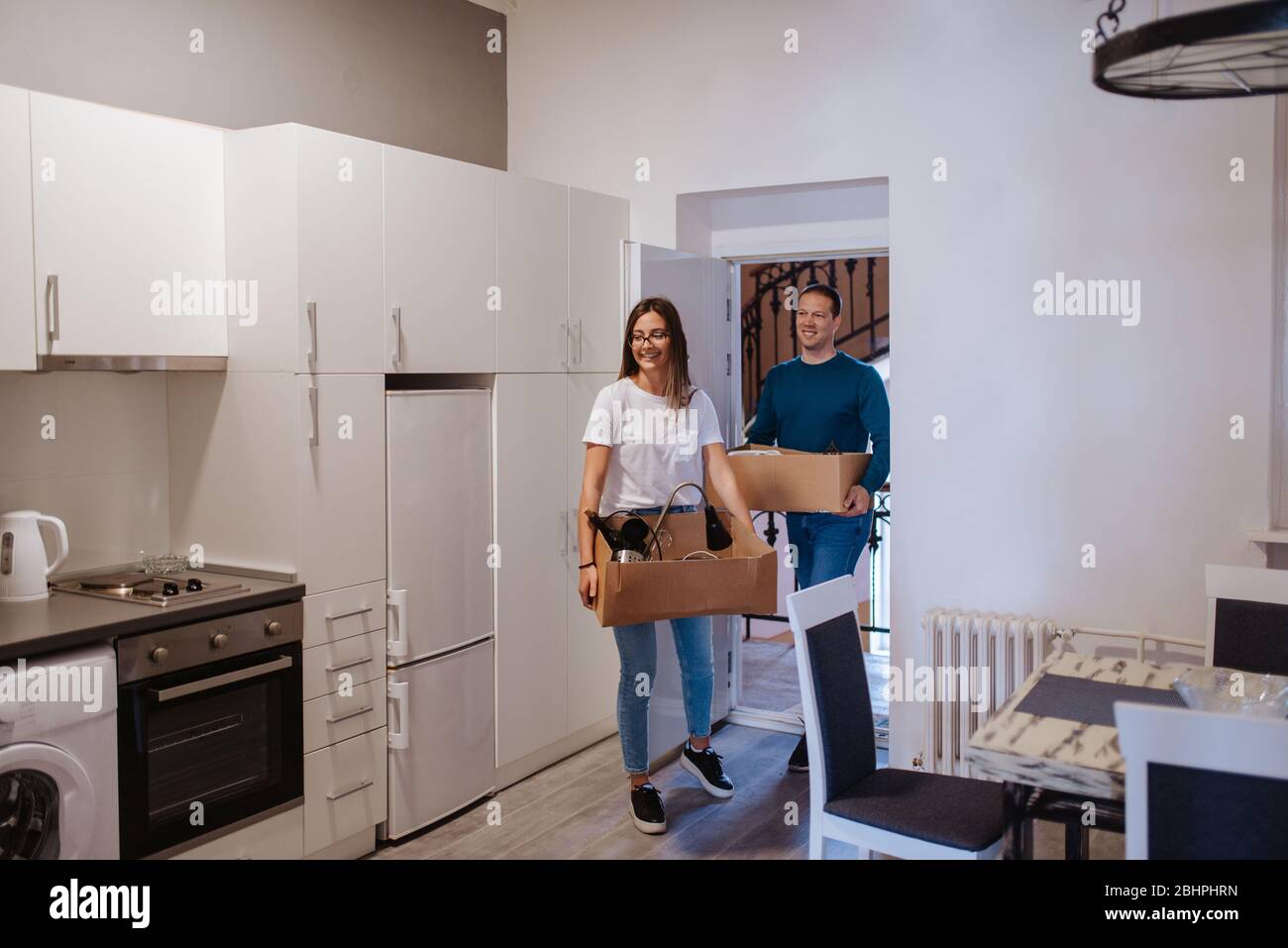Ein attraktiver kaukasischer Mann und eine attraktive Frau betreten eine neue Wohnung mit Schachteln. Ein liebevolles Paar zieht ein Stockfoto
