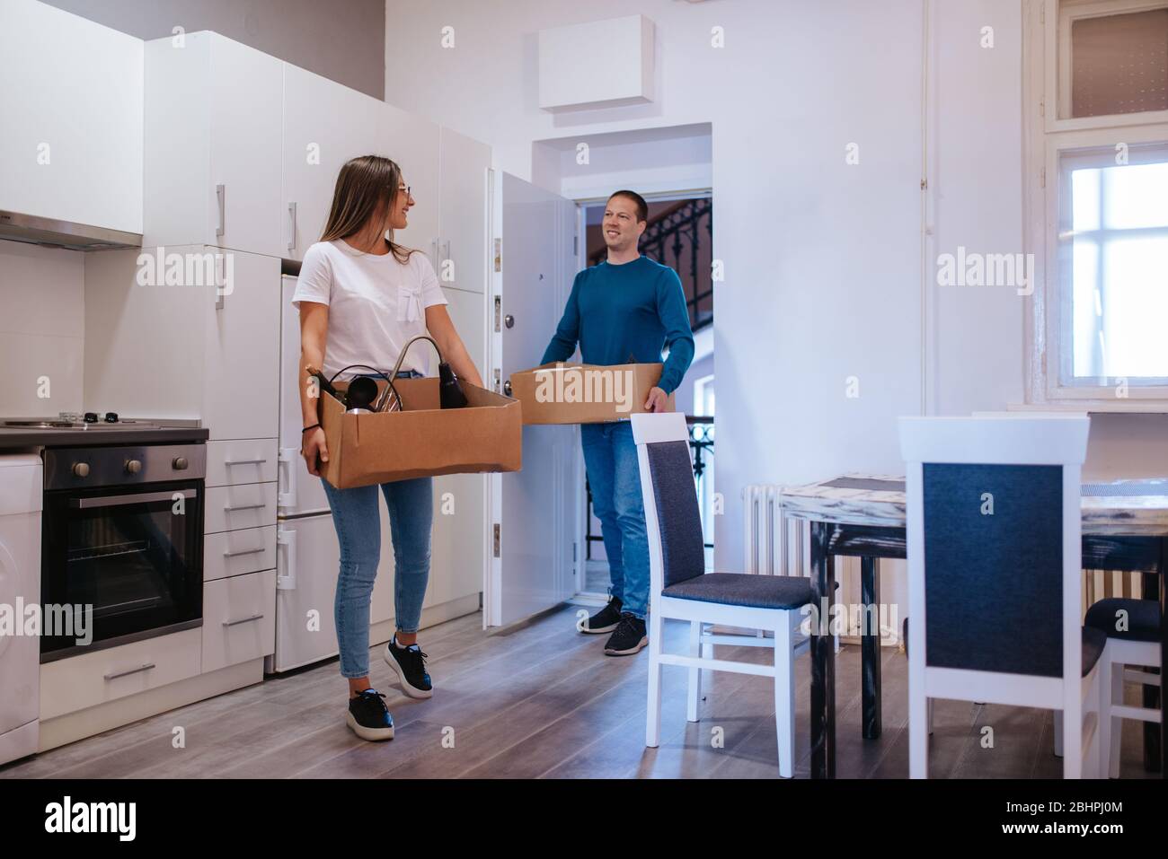Ein attraktiver kaukasischer Mann und eine attraktive Frau betreten eine neue Wohnung mit Schachteln. Ein liebevolles Paar zieht ein Stockfoto