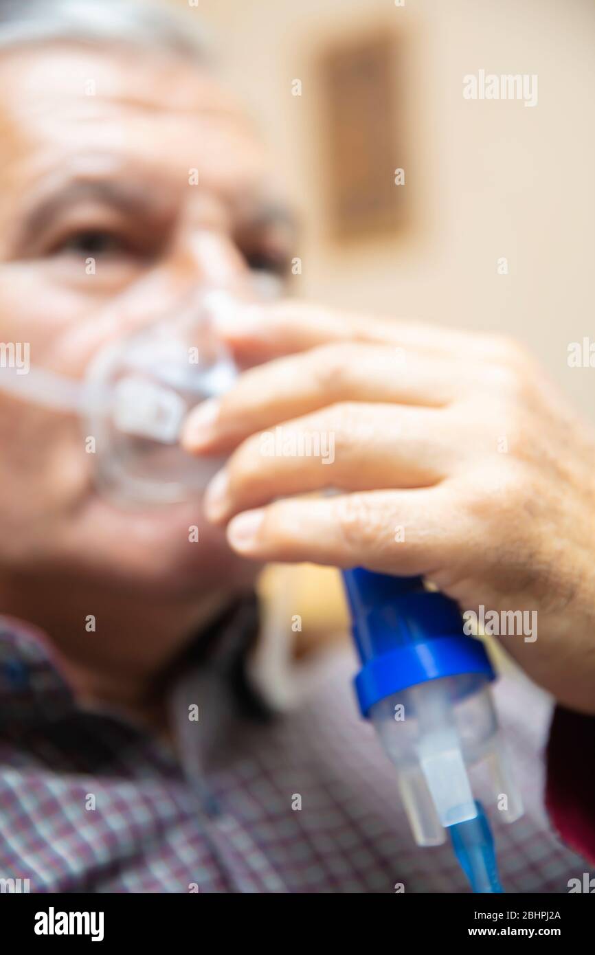 Leitender Mann, der medizinische Geräte für die Inhalation mit Atemschutzmaske verwendet, Vernebler im Zimmer Stockfoto
