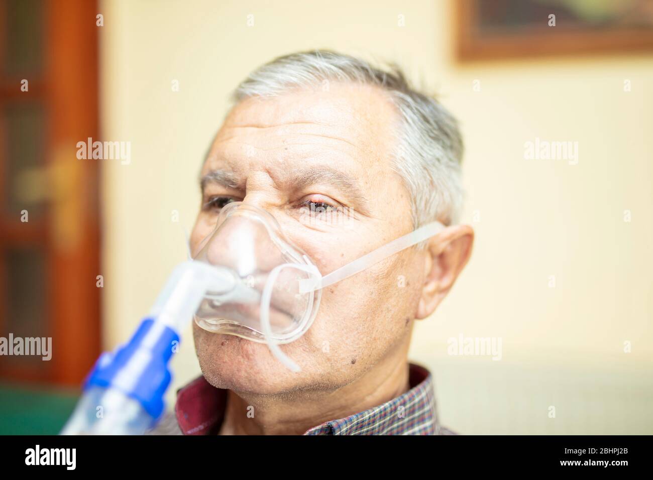 Leitender Mann, der medizinische Geräte für die Inhalation mit Atemschutzmaske verwendet, Vernebler im Zimmer Stockfoto
