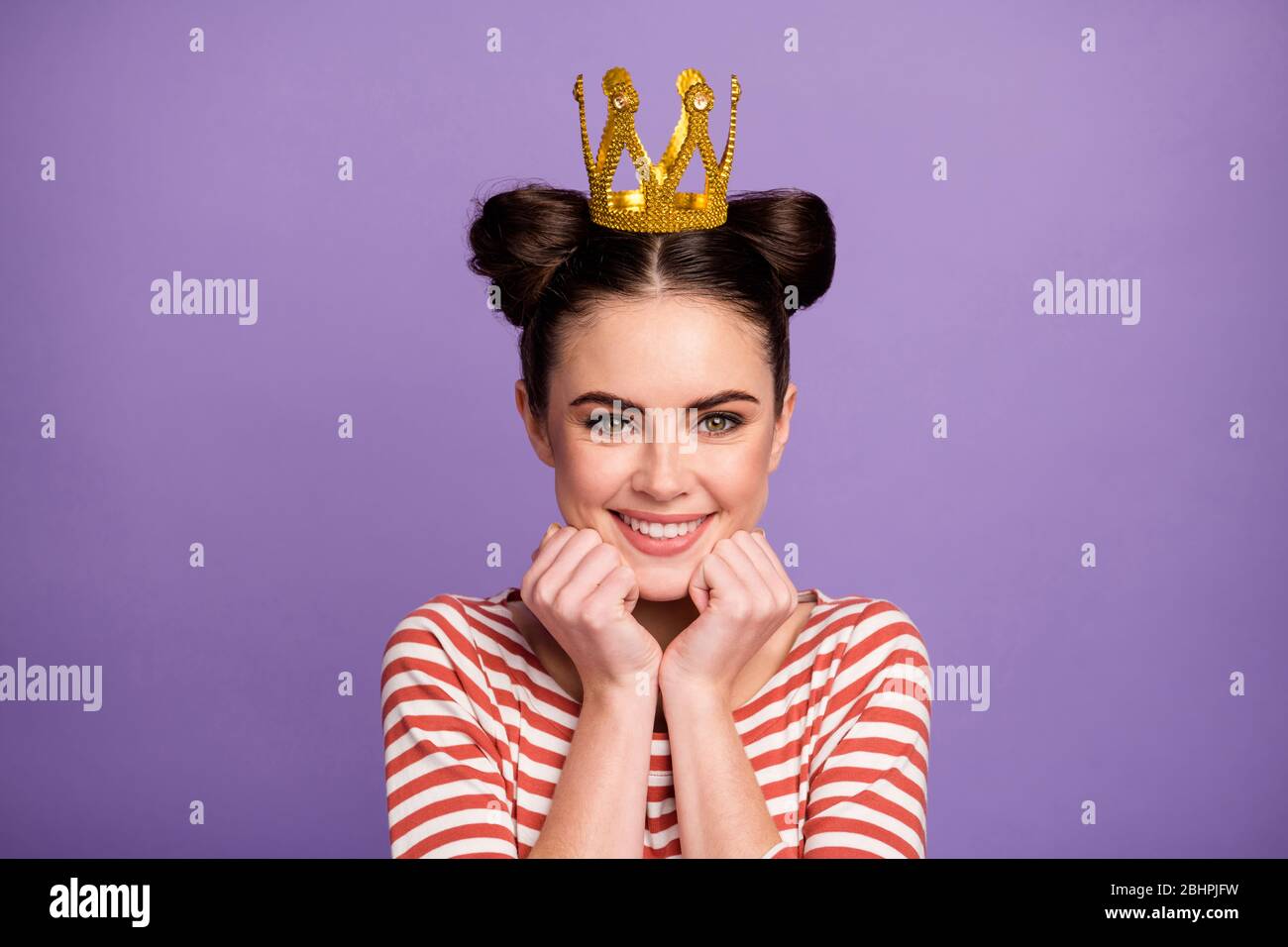 Nahaufnahme Foto von schönen Dame Studenten Abschlussball Königin berühmte Person Arme auf Wangen tragen goldene Tiara weiß rot lässig gestreiften Hemd isoliert Pastell Stockfoto