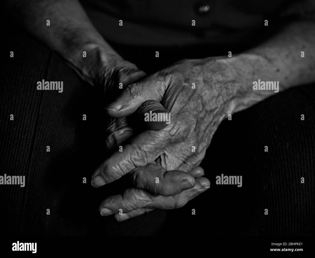 Ältere Frau faltete ihre Hände auf die Knie. Low-Key-Schwarzweißbild Stockfoto