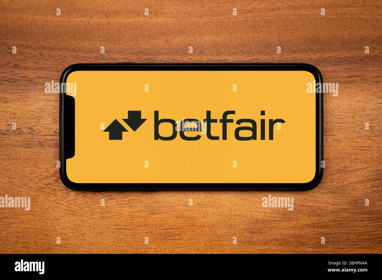 Ein Smartphone mit dem Betfair Logo liegt auf einem einfachen Holztisch (nur für redaktionelle Zwecke). Stockfoto