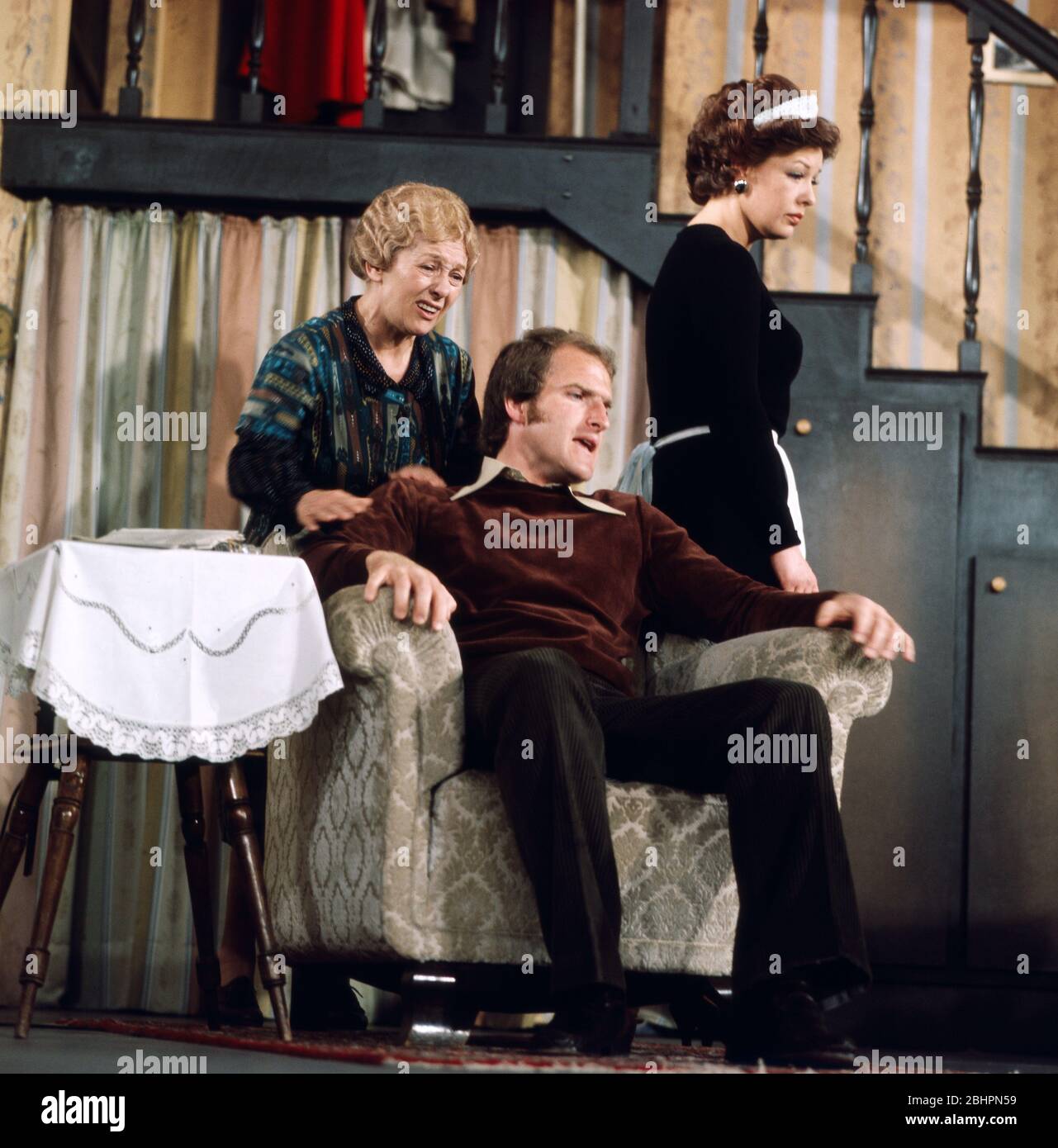 ERNI Singer beschäftigt Bernd Helfrich mit Katharina de Bruyn als Kellnerin gekleidet in das Fenster zum Flur, 1977. ERNI Singer besänftigt Bernd Helfrich neben Katharina de Bruyn in einer Kellneruniform in das Fenster zum Flur, 1977. Stockfoto