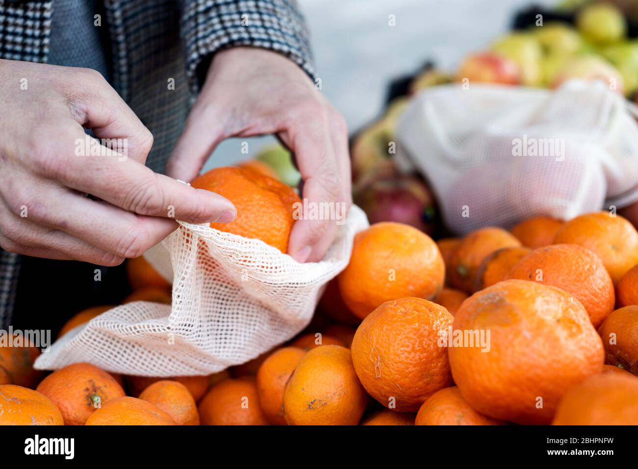 Nahaufnahme eines Mannes, der in einem Greengrocker einkauft und einige Mandarinorangen in einen wiederverwendbaren Textil-Netzbeutel einbringt, um die Kunststoffverschmutzung zu verringern Stockfoto