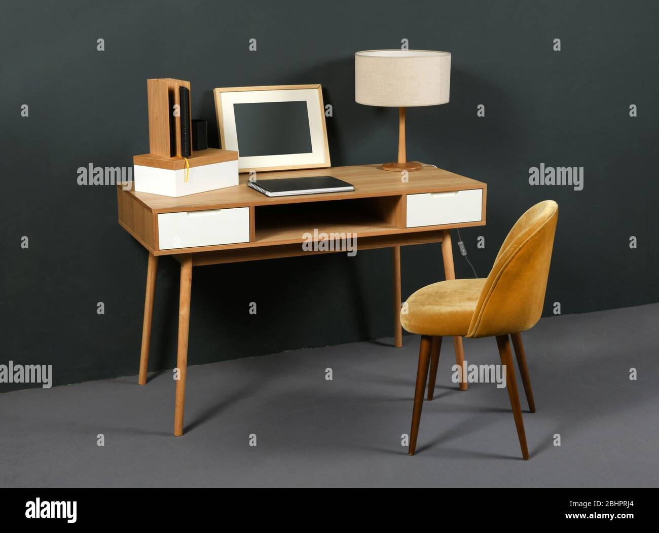 Alter Vintage-Holzschreibtisch mit Retro-Tischlampe, Bilderrahmen und Sessel in einem Raum mit grauer Einrichtung Stockfoto