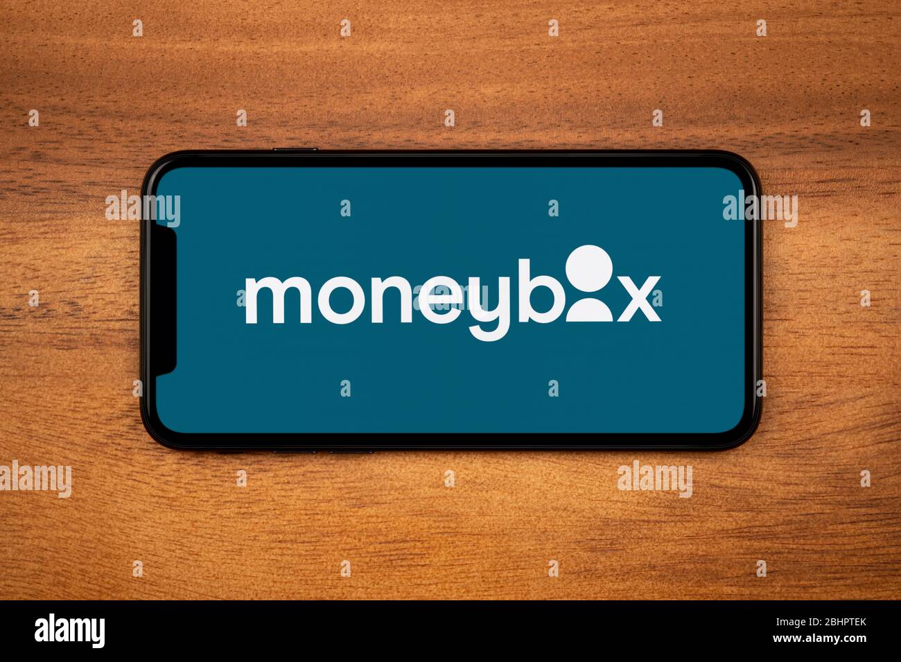 Ein Smartphone mit dem Moneybox-Logo liegt auf einem einfachen Holztisch (nur für redaktionelle Zwecke). Stockfoto