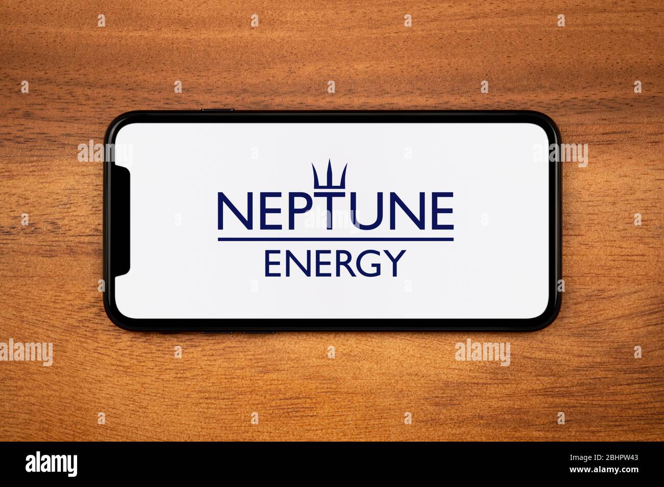 Ein Smartphone mit dem Neptune Energy Logo liegt auf einem einfachen Holztisch (nur zur redaktionellen Verwendung). Stockfoto