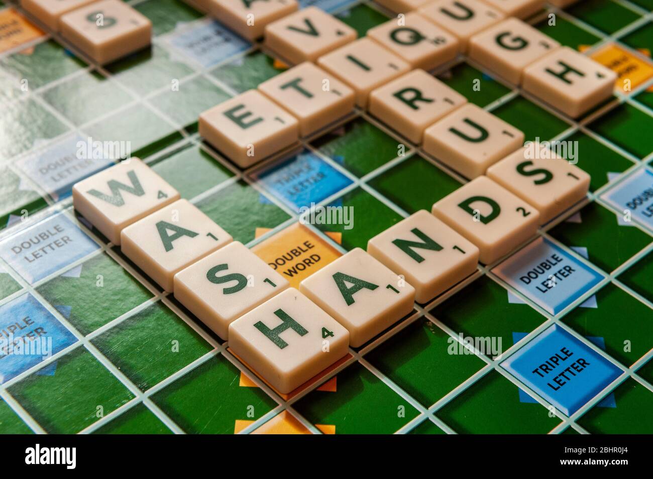 Worte auf einem Scrabble-Brett in Bezug auf die Coronavirus/Covid-19-Pandemie mit 'Wash Hands' im Fokus. Stockfoto
