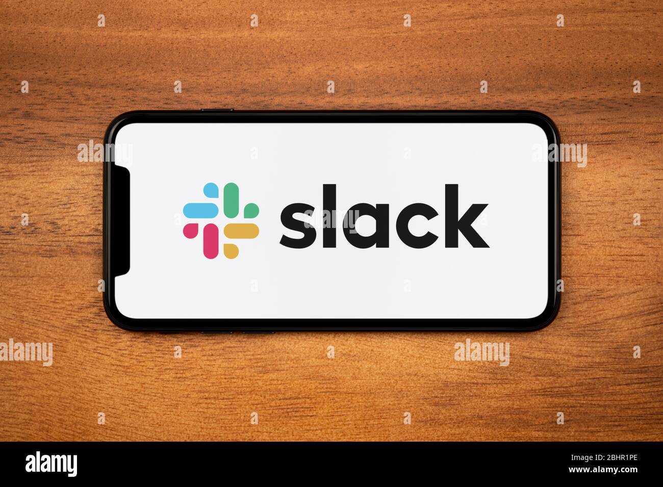 Ein Smartphone mit dem Slack-Logo liegt auf einem einfachen Holztisch (nur für redaktionelle Zwecke). Stockfoto
