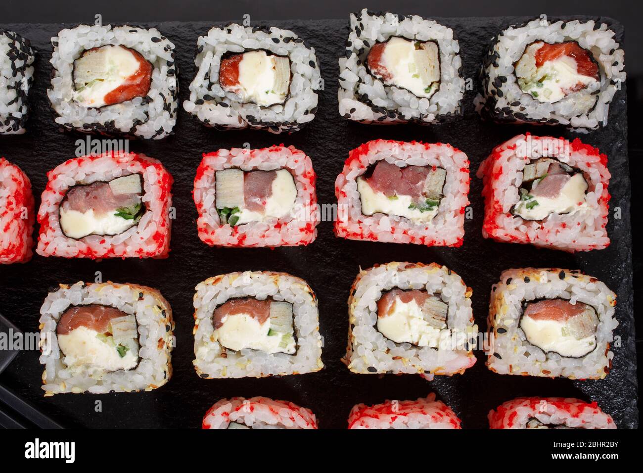 Sushi Roll japanisches Essen im Restaurant. Verschiedene Arten von Sushi-Rollen mit Lachs, Gemüse, Fisch, Kaviar und Sesam auf schwarzem Hintergrund. Stockfoto