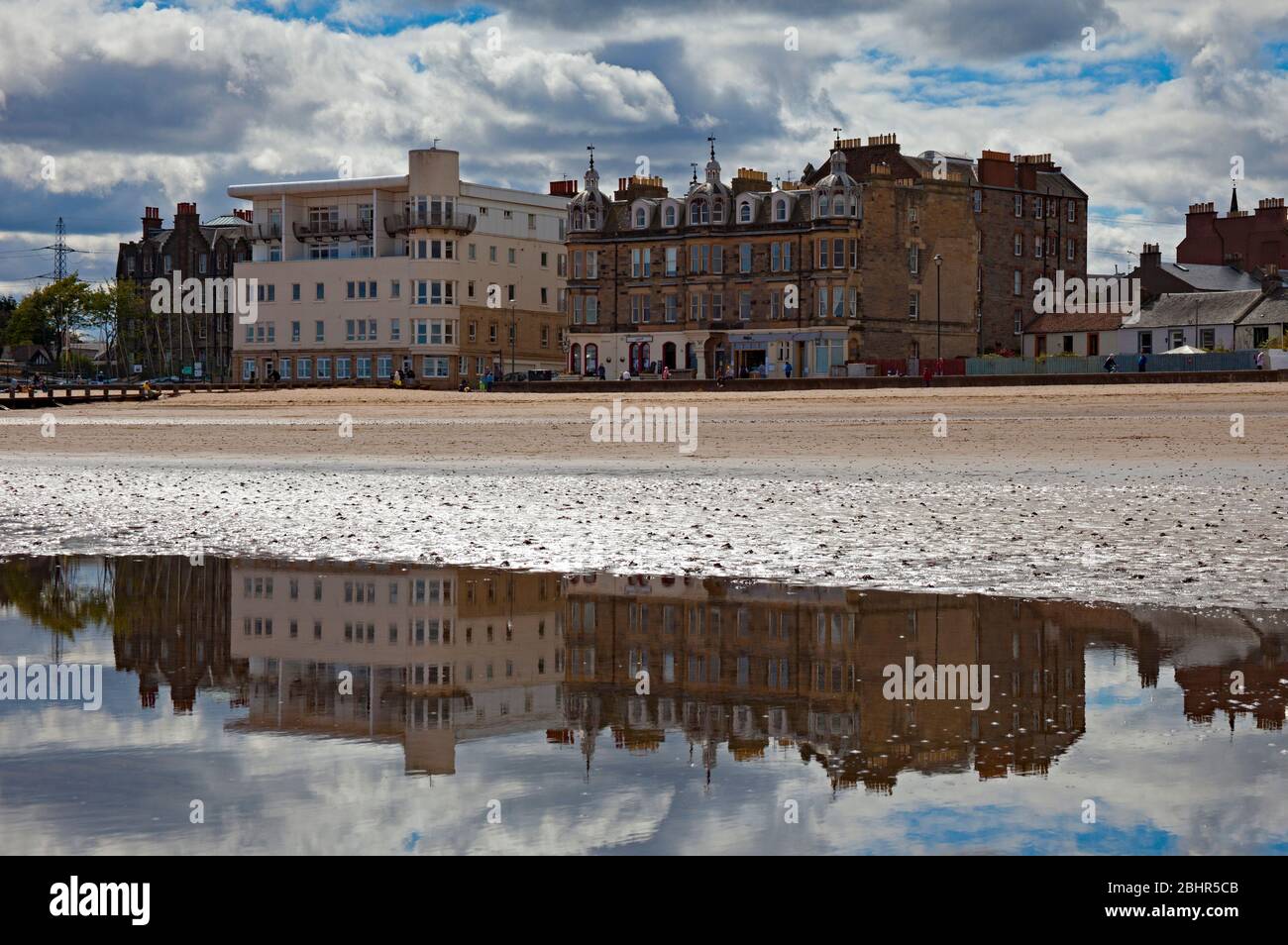 Portobello Beach, Edinburgh, Schottland, Großbritannien. April 2020. Eine Temperatur von 12 Grad mit Sonnenschein und Wolken sehr wenig Wind vor Mittag auf dem sehr ruhigen Strand mit dem gelegentlichen Hundespaziergang und Paare nehmen ihre zulässige Ausübung Zeit, vielleicht reflektieren die letzten 4 Wochen. Polizeiwagen mit zwei Beamten kamen auf der Promenade an und baten kleine Familiengruppen darum, nicht am Strand zu sitzen. Im Bild Porty Architektur spiegelt sich im Meerwasser von ausgehenden Gezeiten. Quelle: Arch White/Alamy Live News Stockfoto