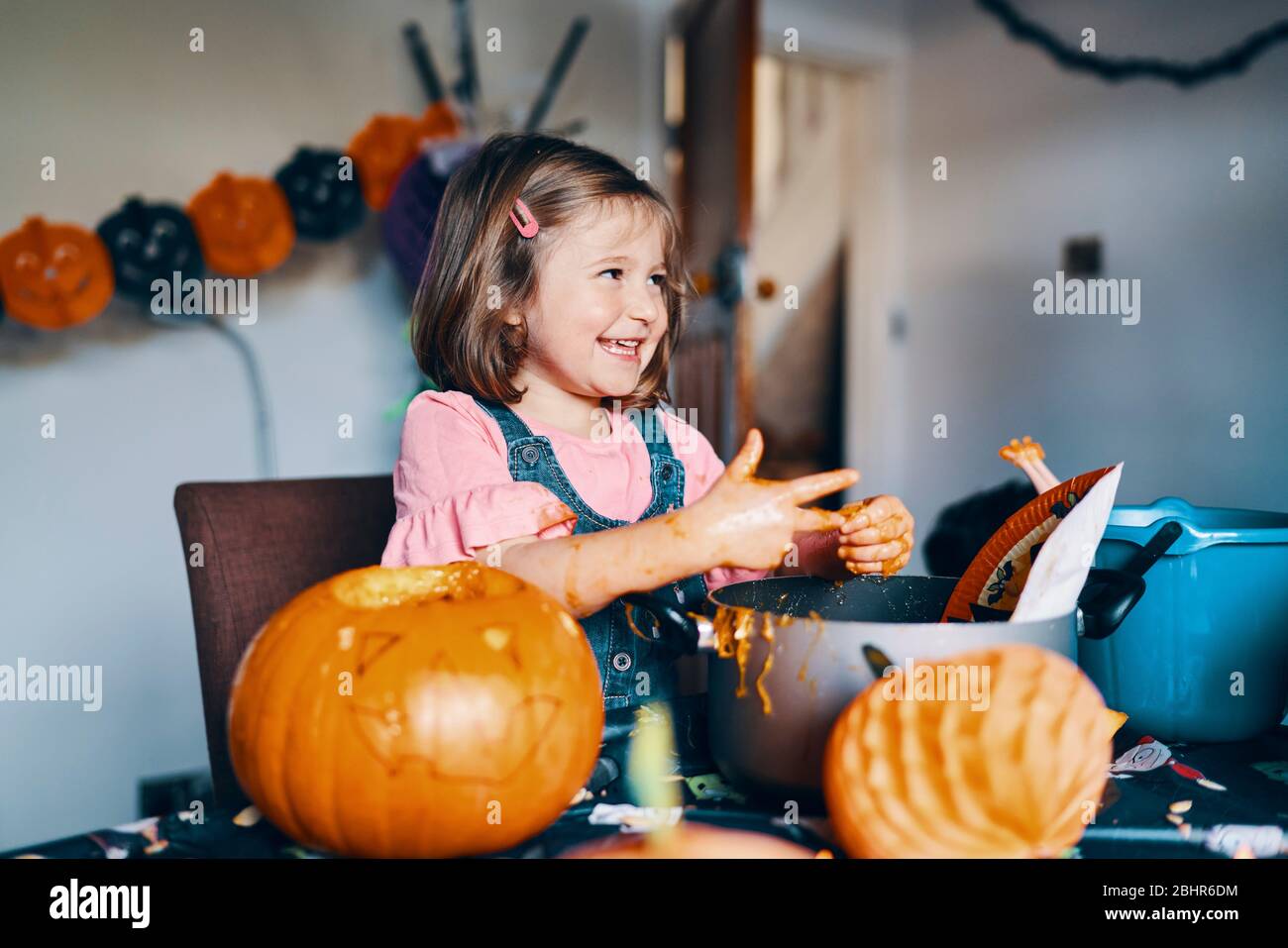Ein lächelndes Mädchen, das die Kürbiskerne und das Fleisch von ihren Fingern nimmt. Stockfoto