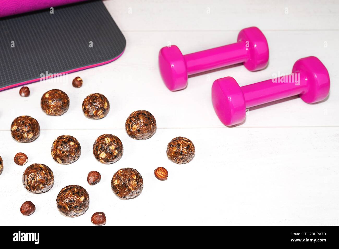 Energiebälle und rosa Hanteln auf hellgrauem Holzhintergrund. Gesunde Fitness und Rohkost Ernährung. Richtige Ernährung Konzept. Selektiver Fokus. Kopierbereich. Stockfoto