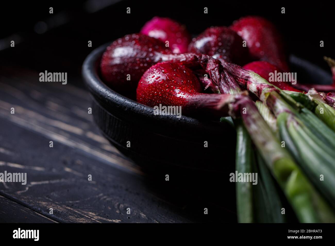 Gespülte spanische Zwiebel in einer tiefen Tonschale auf dunklem Holzgrund. Gemüse in Wassertropfen. Stockfoto